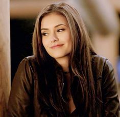 a woman with long brown hair sitting next to a pillar and looking at the camera