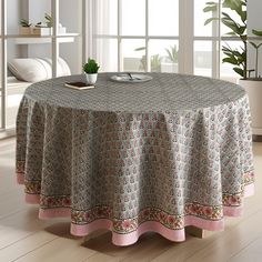 a round table covered with a pink and green paisley print cloth next to a potted plant