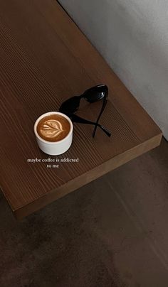 a cup of coffee sitting on top of a wooden table next to sunglasses and eyeglasses