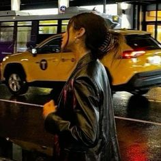 a woman standing in front of a yellow car on a city street at night time