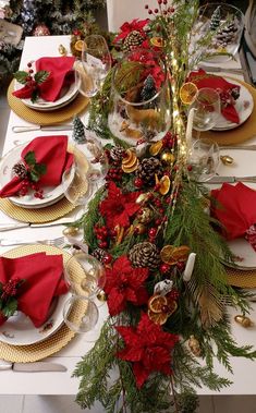 the table is set for christmas dinner with red napkins, pine cones and greenery