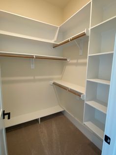 an empty walk in closet with white shelving and brown carpeted flooring is shown