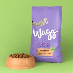 a bag of wags senior dog food next to it's bowl on a green background