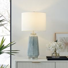 a blue vase sitting on top of a white cabinet next to a lamp and flowers