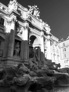 a black and white photo of a fountain in front of a building with statues on it