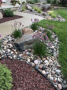 a garden with rocks and flowers in the front yard, along with landscaping plants on either side