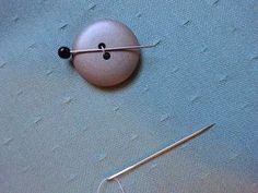 a needle and button on a piece of fabric with pins sticking out of the hole