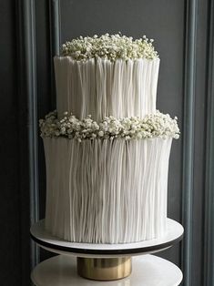 a three tiered cake with white icing and flowers on the top is sitting on a stand