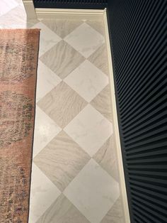 an old rug is laying on the floor next to a black and white tile wall