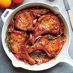 a skillet filled with meat and vegetables on top of a white table next to a spoon