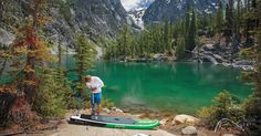 a man standing on top of a surfboard next to a lake