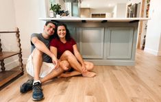 a man and woman sitting on the floor in front of a kitchen island with stairs