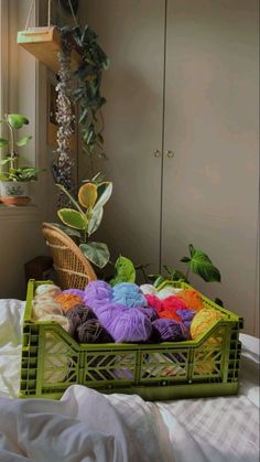 a basket filled with yarn sitting on top of a bed next to a mirror and potted plant