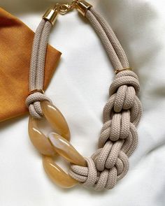 a beige necklace with an orange tie on top of white sheets and a gold clasp