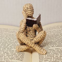 a small wooden figurine sitting on top of an open book holding a book