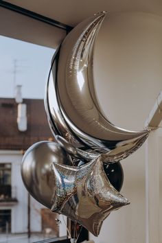 some silver balloons are hanging from the ceiling in front of a window with a house behind them