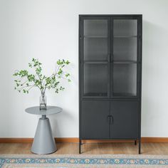 a black cabinet next to a table with a vase on it