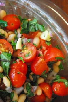 a salad with tomatoes, beans and spinach in a glass bowl