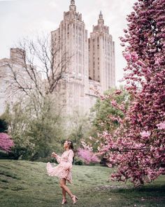 a woman in a pink dress is walking through the grass near some trees and buildings