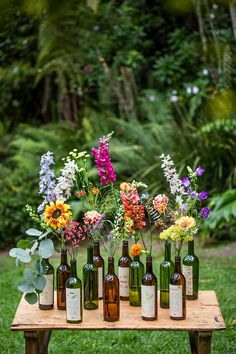 a wooden table topped with lots of bottles filled with different types of flowers and greenery