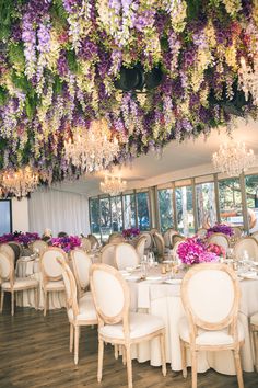 the dining room is set up with white linens and purple flowers hanging from the ceiling