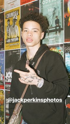 a young man holding his hand out in front of a wall covered with posters