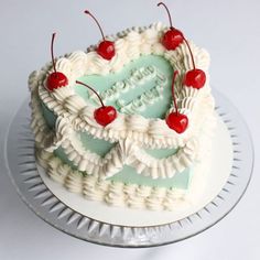 a heart - shaped cake with cherries on top is sitting on a glass plate