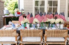 an outdoor table with american flags on it and flowers in vases at the center