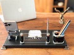 a desk with a cell phone, pen and pencil holder on it next to an apple laptop