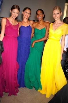 four women in colorful dresses standing next to each other with one woman wearing a yellow dress