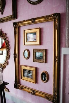 a pink wall with gold framed pictures on the wall and a mirror hanging above it