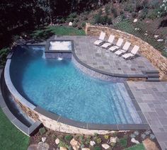 an aerial view of a swimming pool surrounded by grass and rocks, with lounge chairs around it