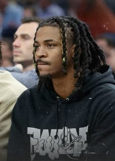 a young man with dreadlocks sitting in front of a basketball court while wearing a black hoodie