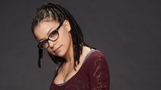 a woman with dreadlocks and glasses looking at her cell phone while standing in front of a dark background