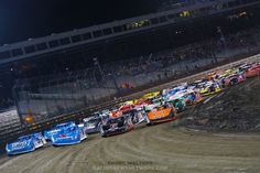 a group of cars that are sitting in the dirt at a race track with people watching