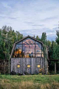 an old barn sits in the middle of a field with trees and grass around it