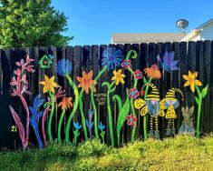 a wooden fence with flowers painted on it and two cats sitting in the grass next to each other