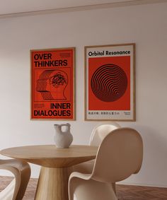 two posters hang on the wall above a round table with chairs and a vase in front of it