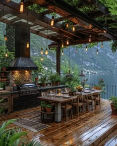 an outdoor kitchen and dining area on a deck overlooking the water with mountains in the background