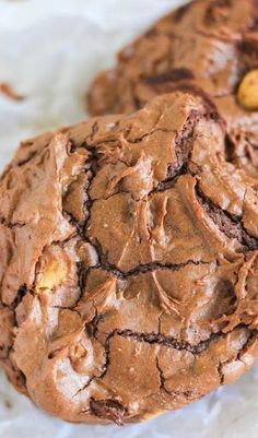 two chocolate cookies with peanut butter in the middle on top of white paper and one is half eaten