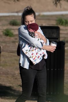 a woman holding a baby in her arms while standing next to a trash can and tree