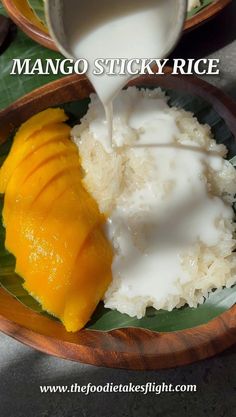 mango sticky rice with milk being poured into it on a wooden plate next to a banana leaf