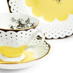 two tea cups and saucers with yellow flowers on the rims, one is black and white