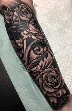 a black and grey tattoo with roses on the arm, eye in the center surrounded by leaves