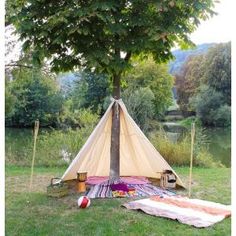 a teepee sitting under a tree next to a lake