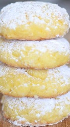 a stack of three lemon filled donuts on top of a wooden table with powdered sugar