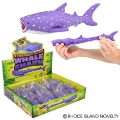 a hand holding a purple shark toy in front of a box