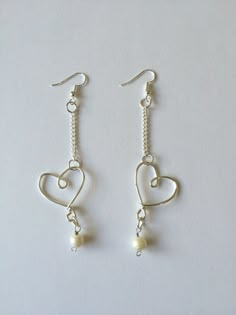 two heart shaped earrings with pearls hanging from the hooks on a white tablecloth background