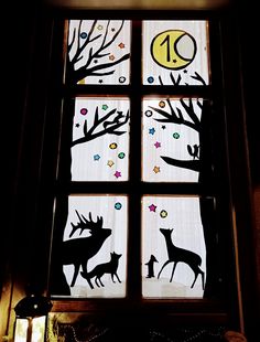 the window is decorated with black silhouettes of deer, trees and moon on white paper