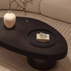 a black coffee table with a white vase sitting on it's top in front of a couch